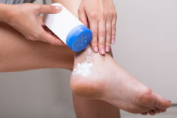 A woman puts talcum powder on her foot.