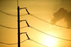 The sun rises behind a set of power lines.