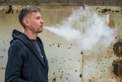 Young man vaping next to a wall