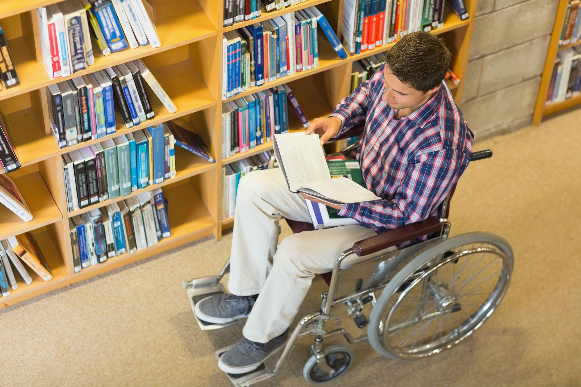 A man in a wheelchair reads a book in a library.