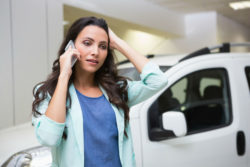 A woman at a car dealership talks on the phone.