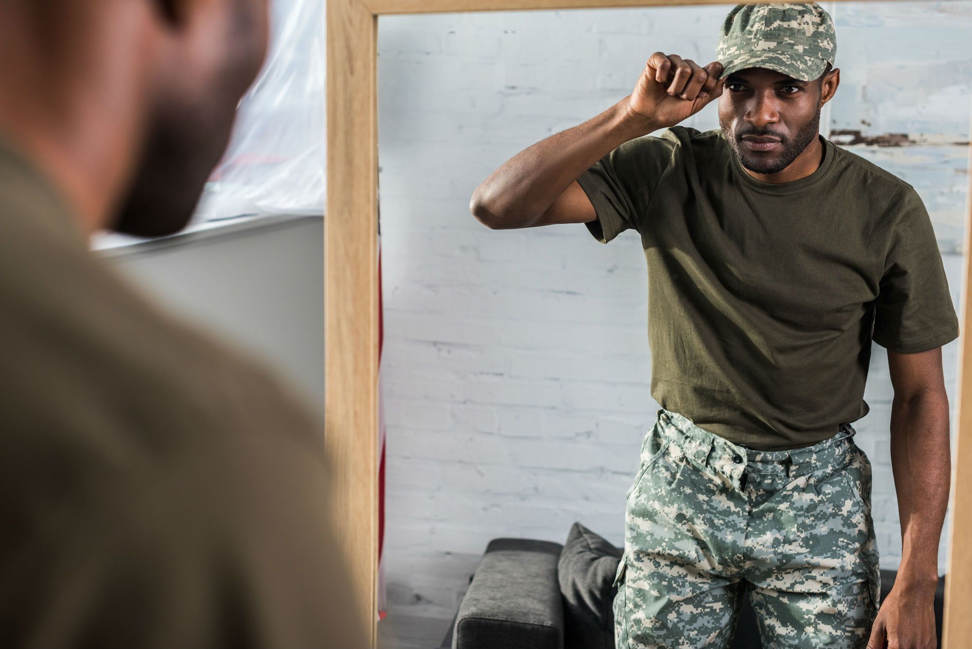 Young African American Army member in camo hat admires his look in the mirror.