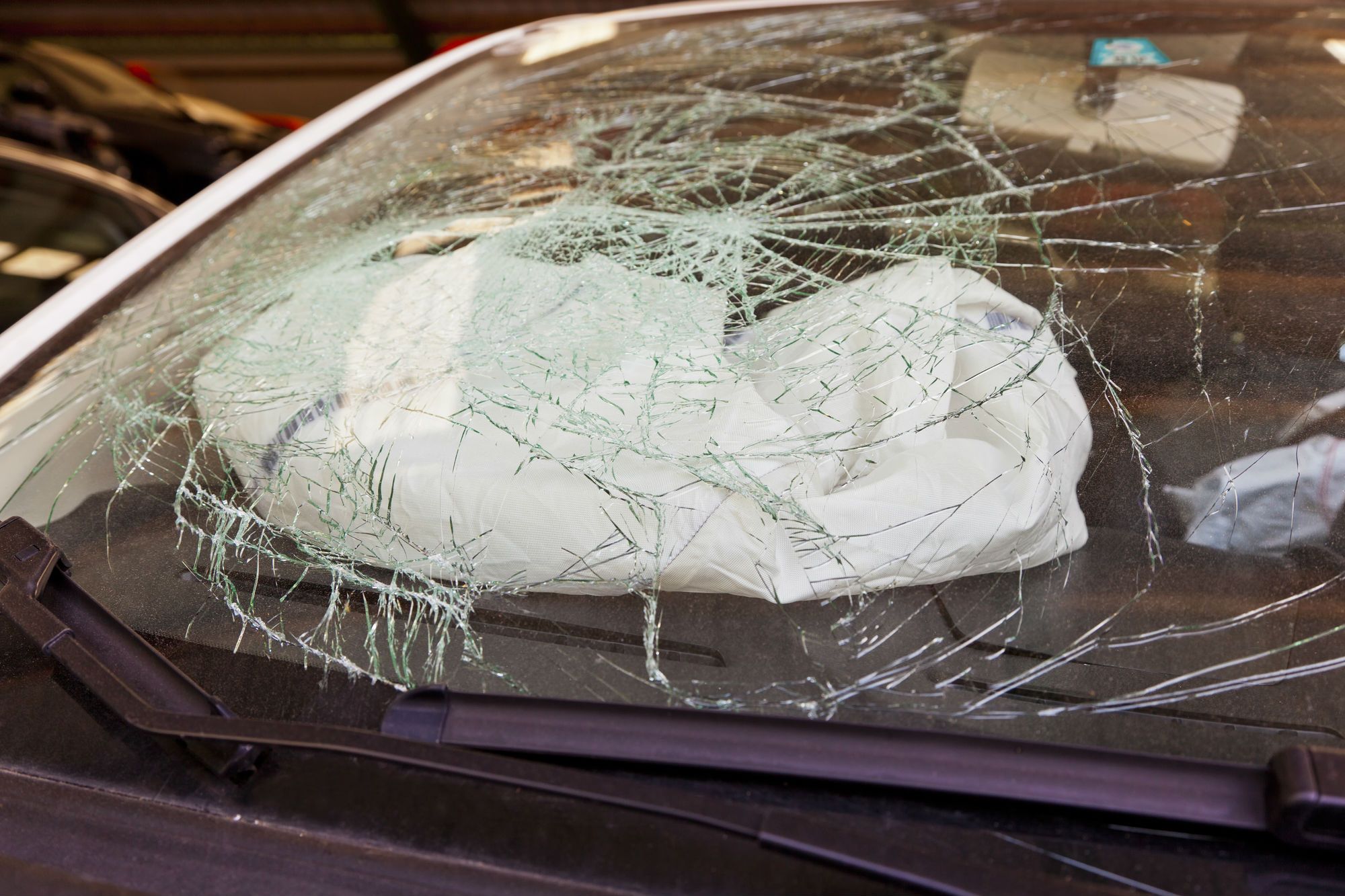 Closeup of deployed airbag behind broken windshield of crashed car
