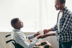 African American young man hands cup of coffee to his dad in a wheelchair