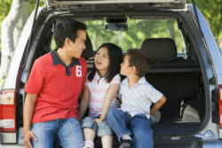 Dad and two young kids sit on back of opened minivan.