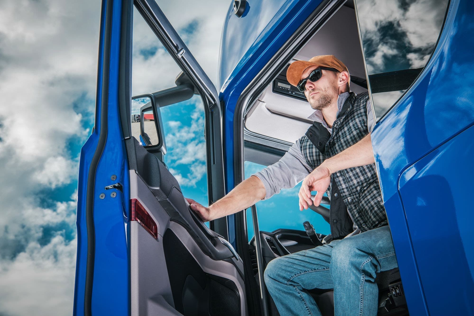 Male trucker in flannel shirt exiting cab of big blue commercial semi truck.