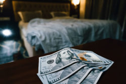 Several hundred dollar bills sit on a dresser with a blurred hotel bed in the background.