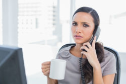An irritate businesswoman looks at the camera as she's on a frustrating call.