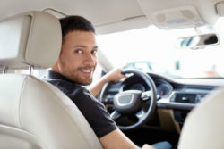 Man looks over shoulder to back seat as he has hand on steering wheel.