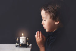 Small boy prays in front of lit candle.