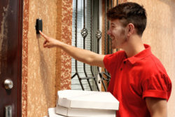 A young man rings a doorbell to deliver pizzas at a home.