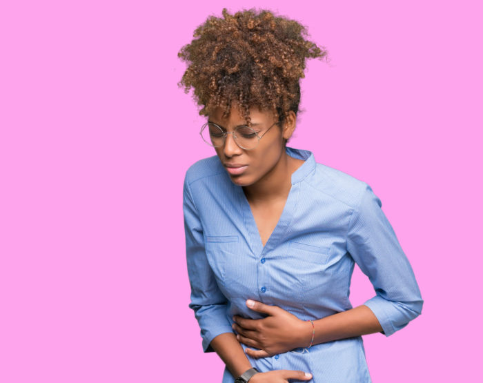 Young woman stands holding her stomach in pain
