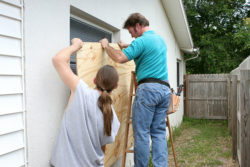 Two men apply plywood to a window in preparation for a hurricane