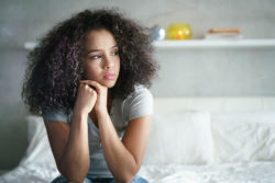 A depressed young woman sits on the edge of a bed.