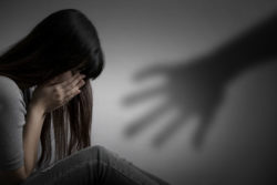 Depressed young woman sits on floor with head in hands as a shadow of a large hand approaches her