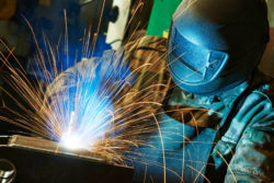 Fully suited up welder creates sparks working at factory