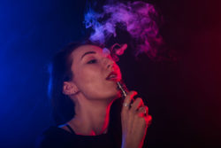 Woman vapes with neon lighting in background