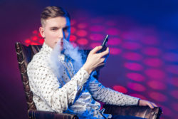 Stylish young man sits in fancy chair and vapes