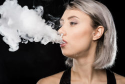 A young woman breathes out a cloud of vapor.