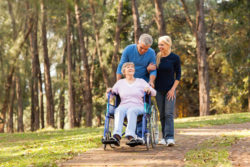 Mature couple takes mom in wheelchair for walk in the woods