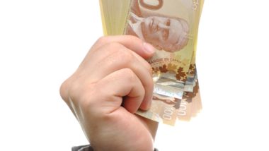 Hand holding money regarding the massive $107 billion aid package passed to help Canadians as they cope with job losses and other economic challenges during the COVID-19 pandemic