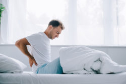 man on bed holding back and grimacing