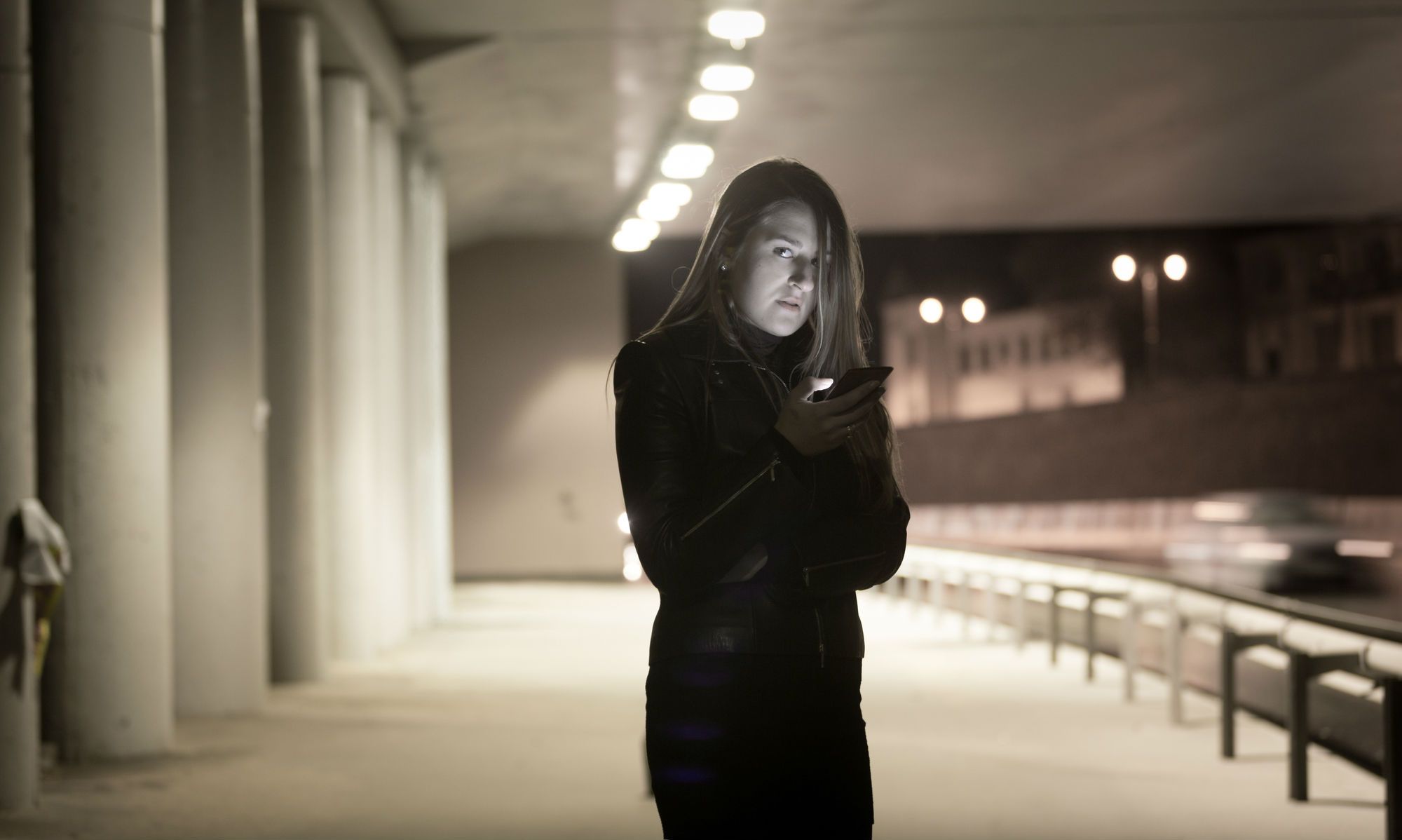 Woman stands on dark street with her cell phone