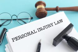 Pair of glasses, gavel, rubber stamp, pen and paper that says Personal Injury Law