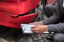 Closeup of male insurance adjuster checking damaged car bumper