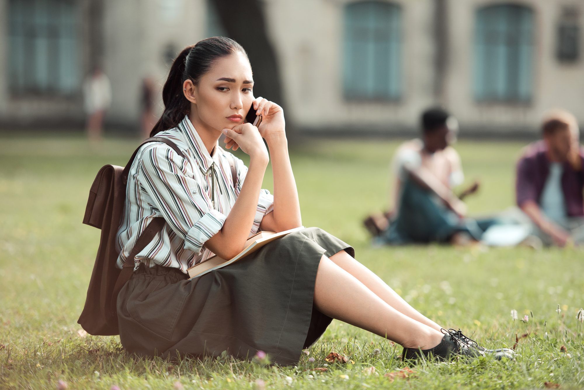 Upset female college student talks on cellphone while sitting on lawn