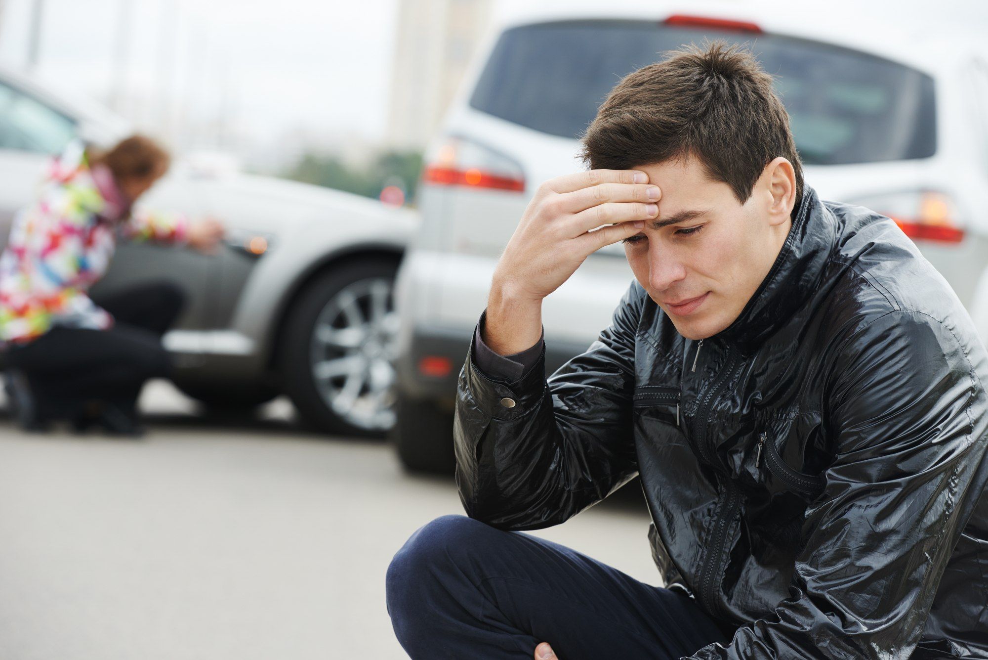 Young man appears upset and sits on curb after car accident