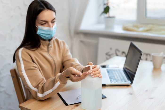 woman with hand sanitizer and wearing a face mask while working