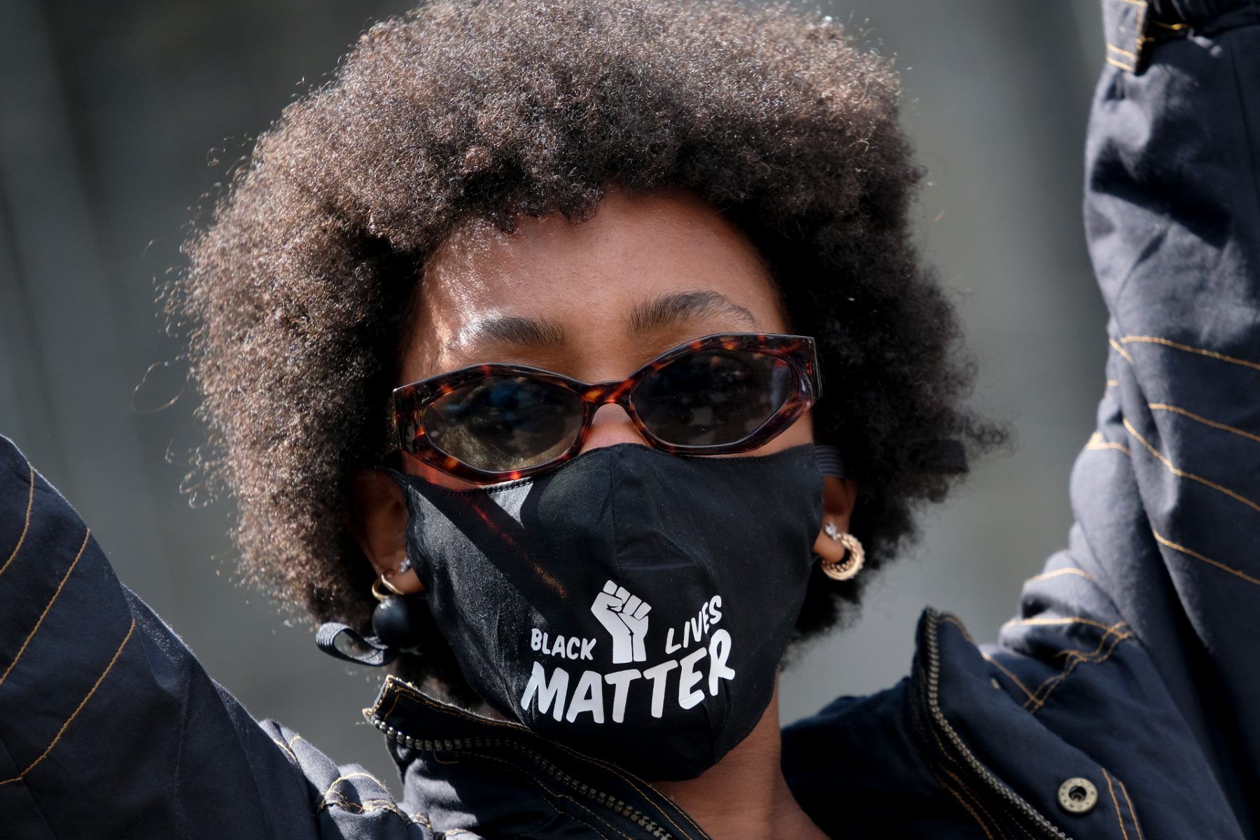 Protester wearing sunglasses and a face mask that reads "Black lives matter" with an image of a fist