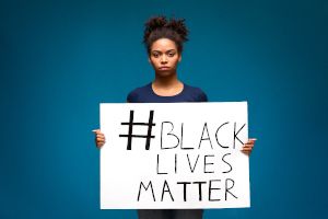 Protester in front of teal background holds sign that reads "#Black Lives Matter"