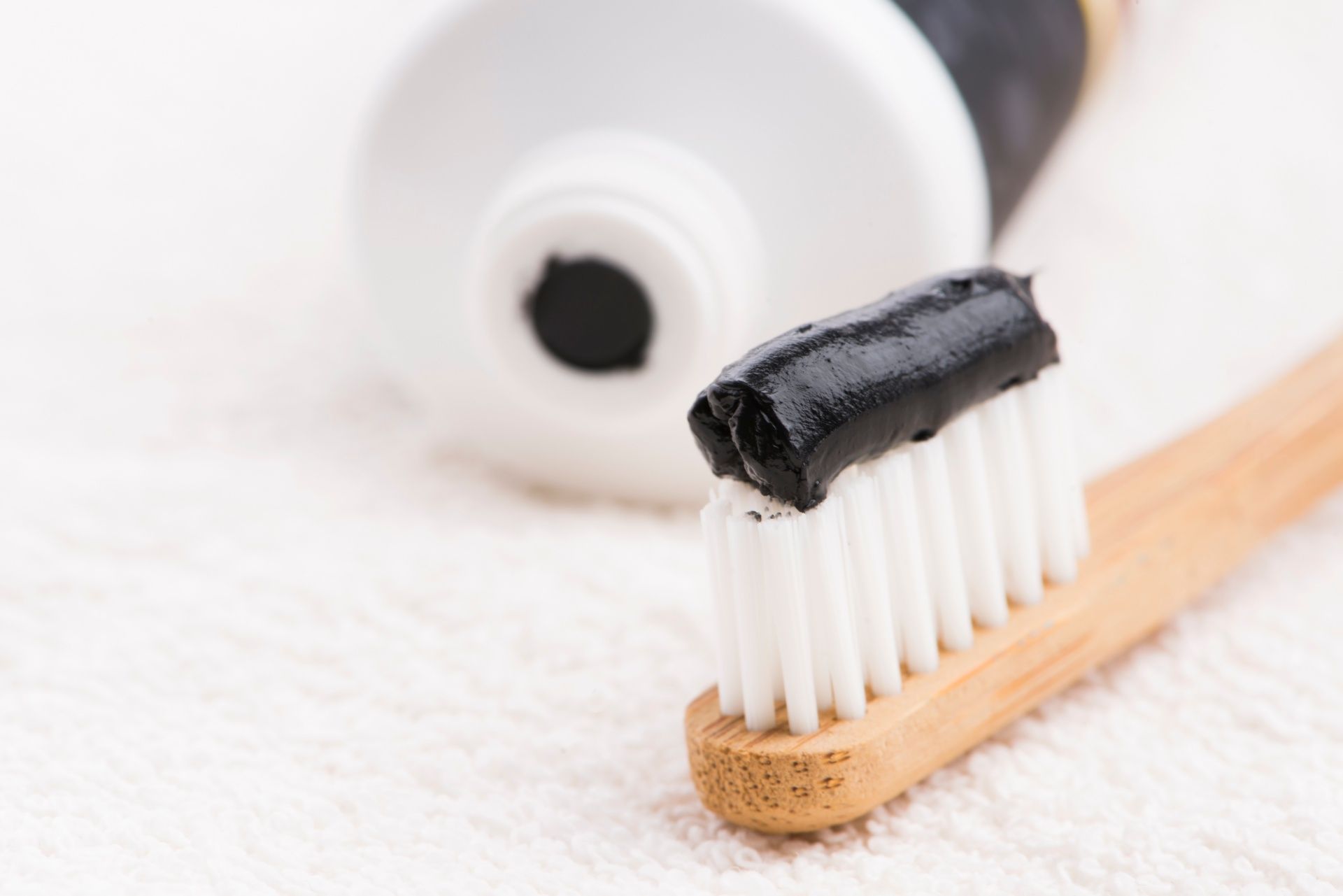 Charcoal toothpaste on a wooden toothbrush with the tube int he background