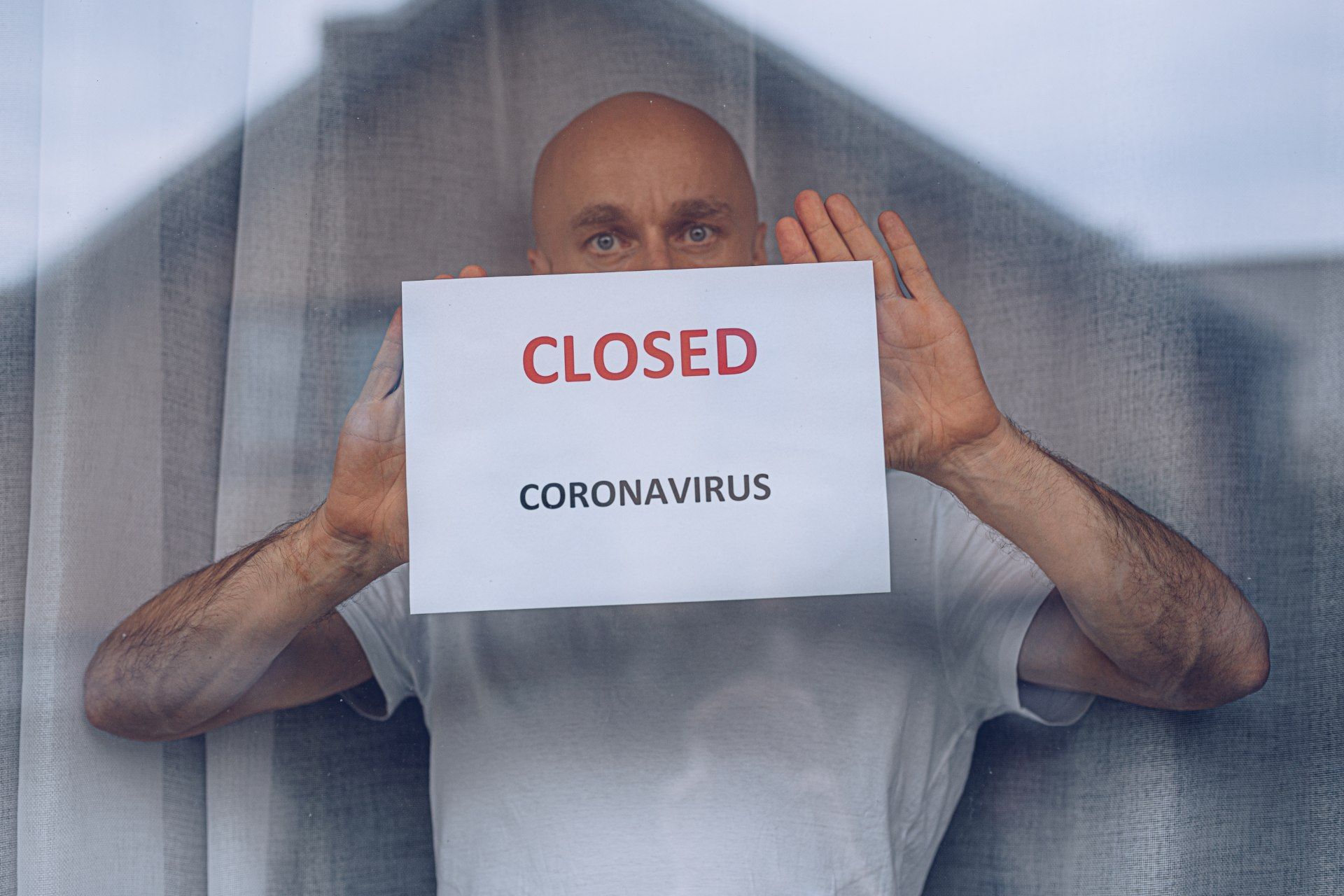 Man standing in window with paper that reads "CLOSED CORONAVIRUS"
