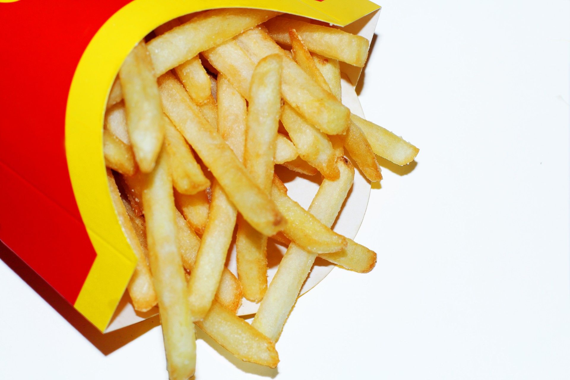French fries in a red-and-yellow fast-food container, lying on white background