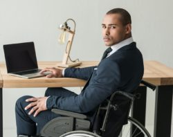 Man in wheelchair sits at desk with laptop