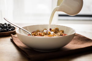 Milk being poured from pitcher over white bowl of cereal and spoon