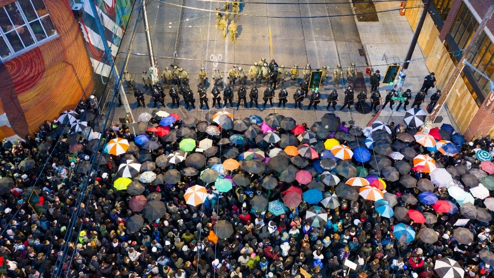Seattle protesters with umbrellas face a line of police officers in riot gear
