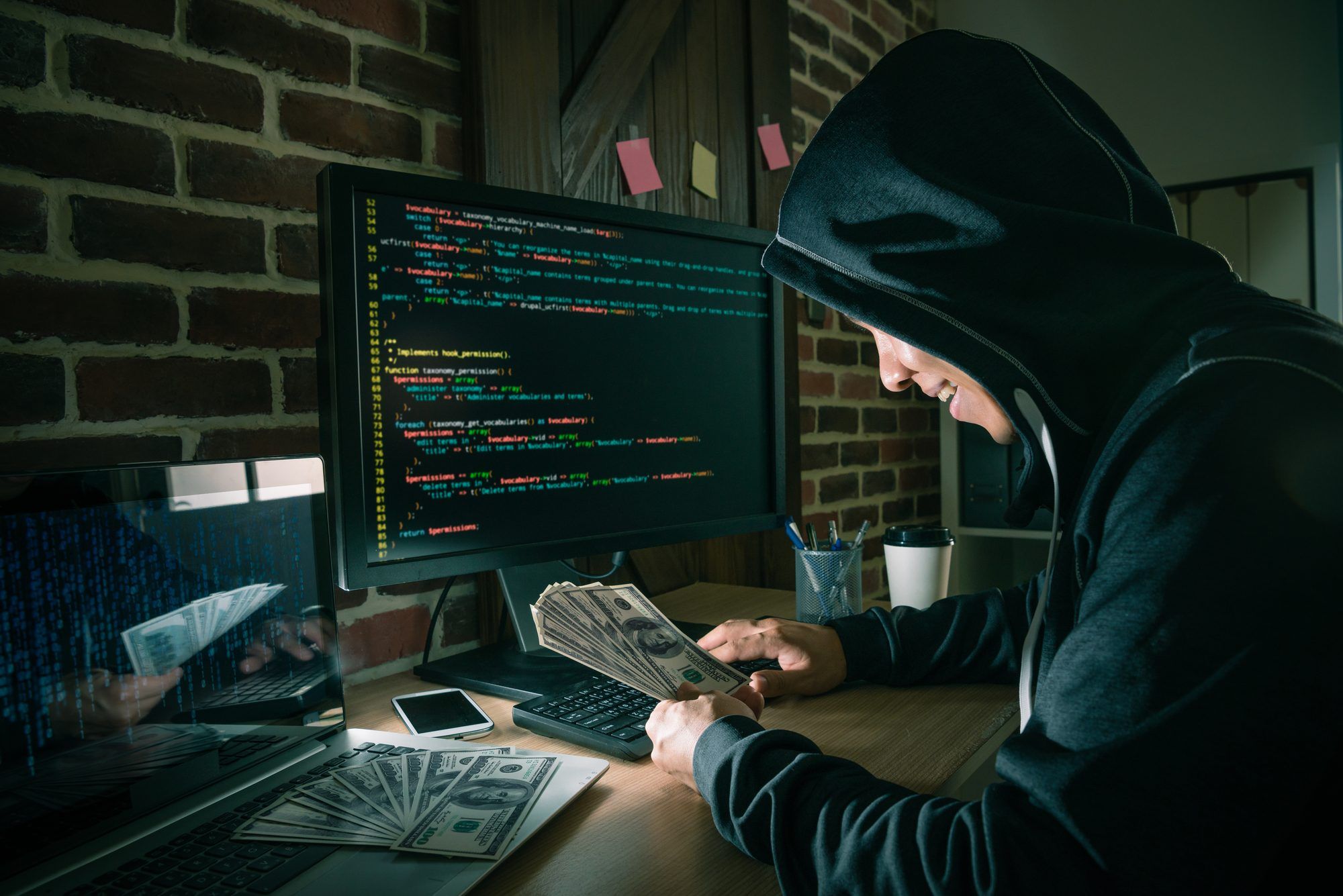 Smiling hacker counts money while sitting in front of computer monitor