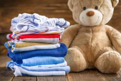 Teddy bear and stack of baby clothes on wood floor