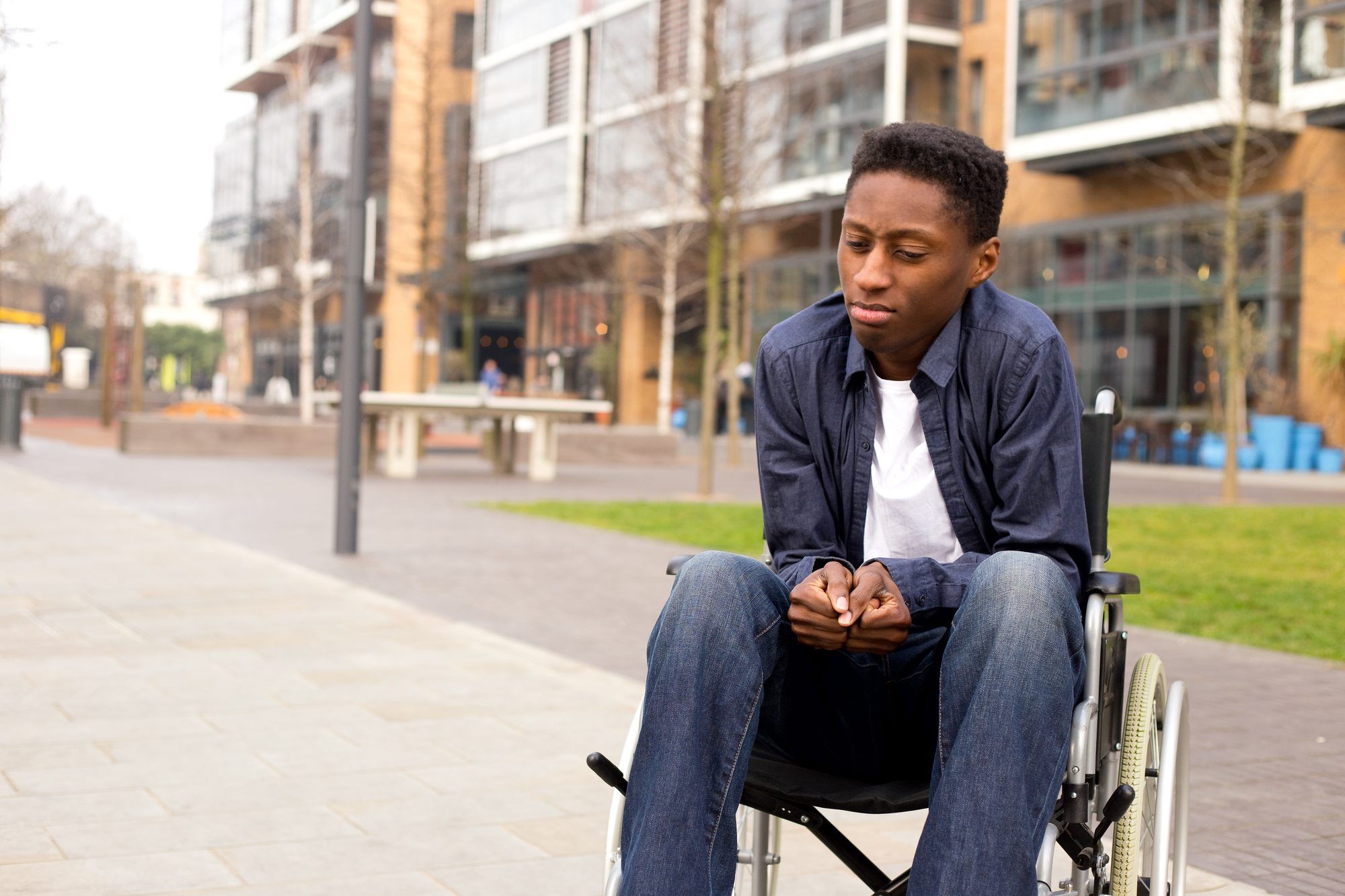 Young man sits in wheelchair on sidewalk