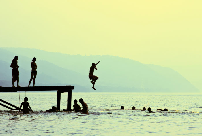 teens jumping off of a dock into a lake at a Jewish summer camp