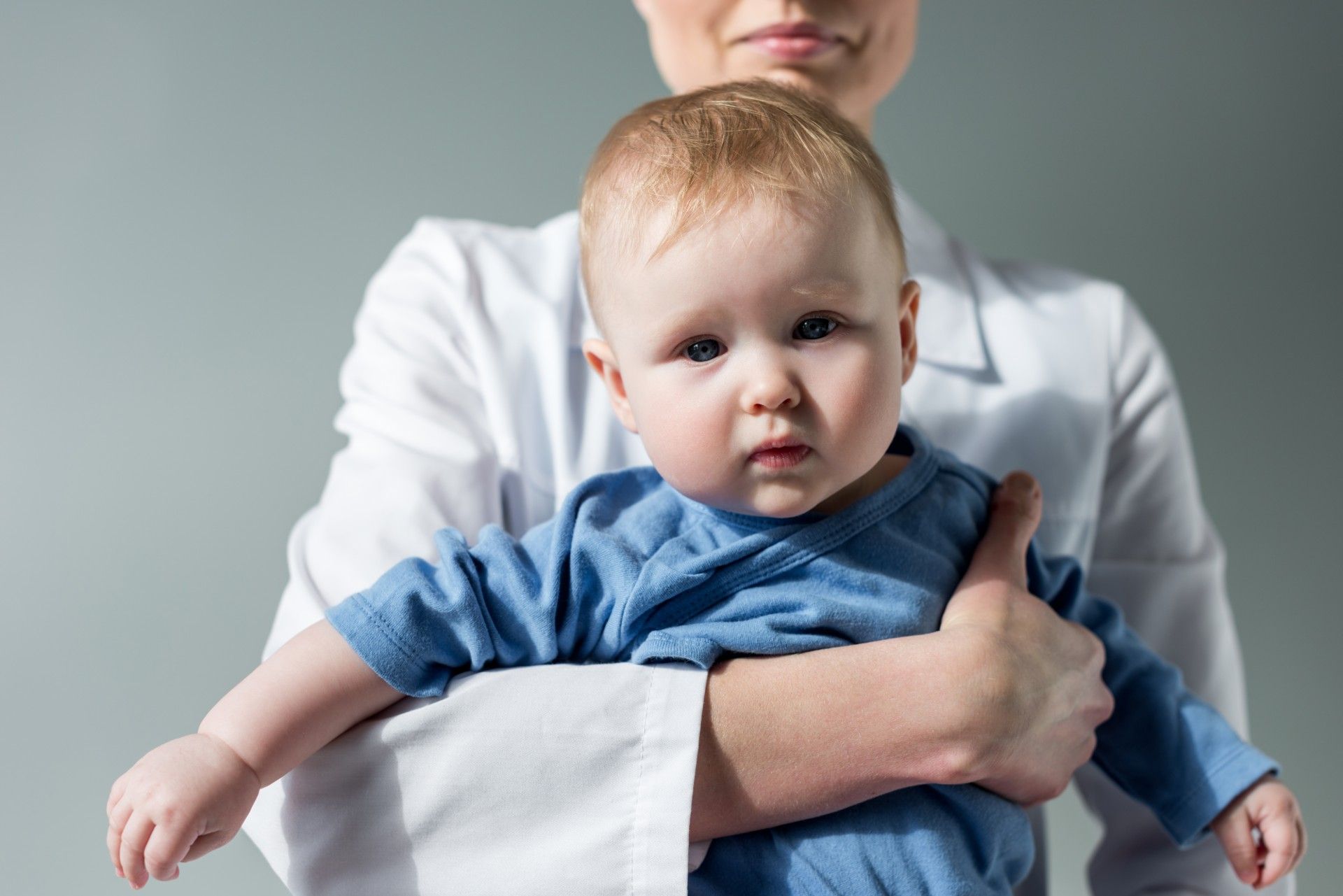 Woman in white lab coat holding a baby in a blue onesie
