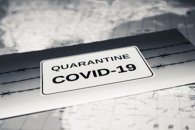 Black-and-white image of "Quarantine COVID-19" sign on barbed wire with map in the background