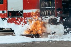 Closeup of fire being hit by foam and nearby firetruck 