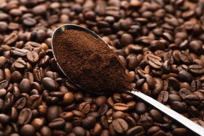 Ground coffee in a spoon with whole coffee beans in the background - Kroger coffee