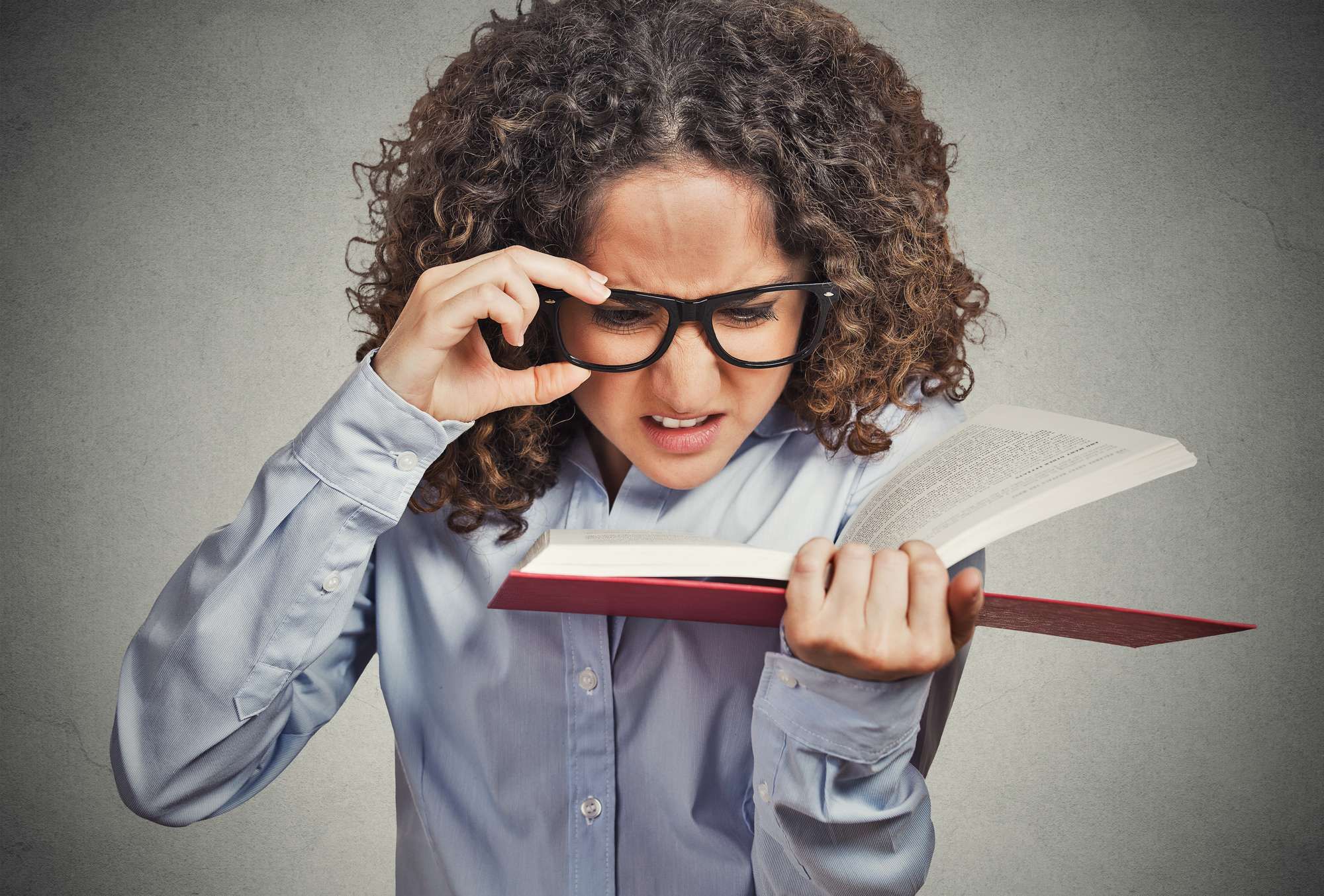 Woman adjusts glasses while trying to read book