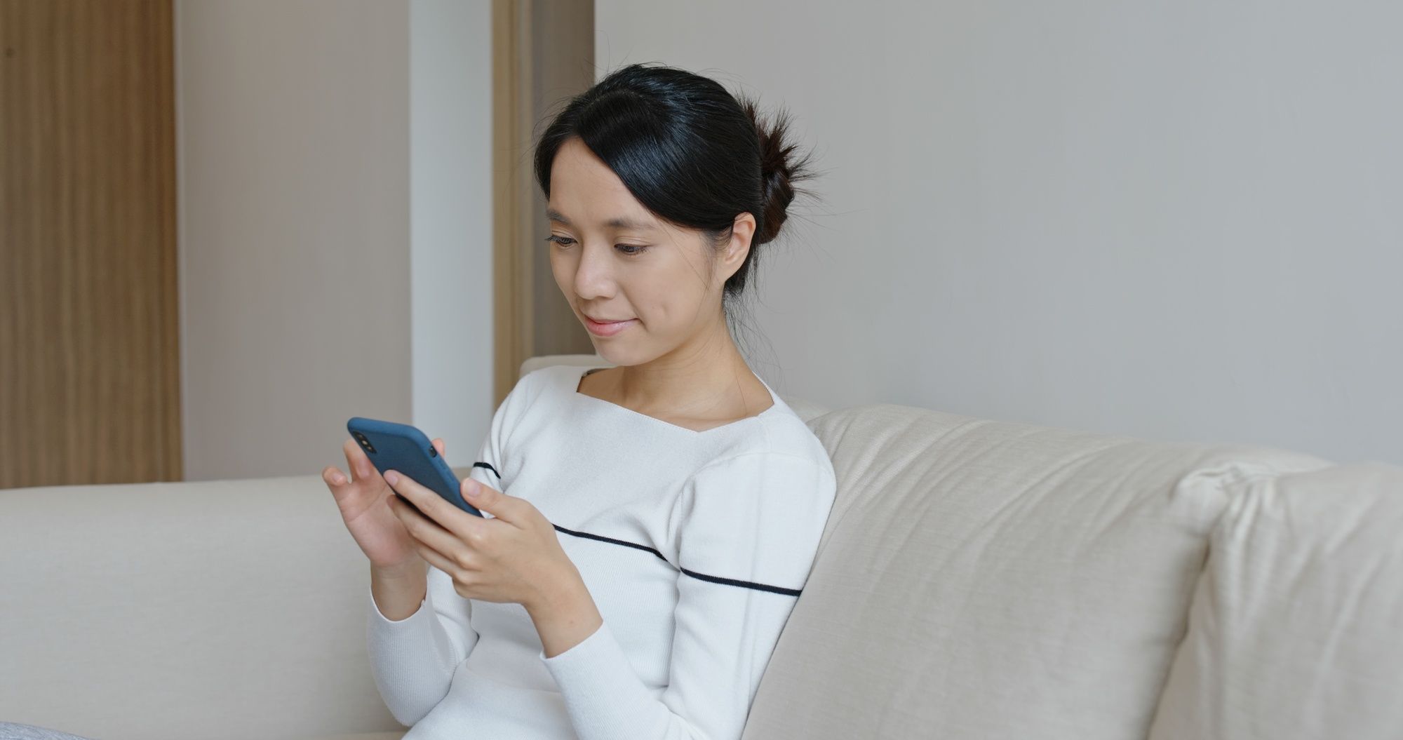 Woman sits on couch and reads texts on cell phone